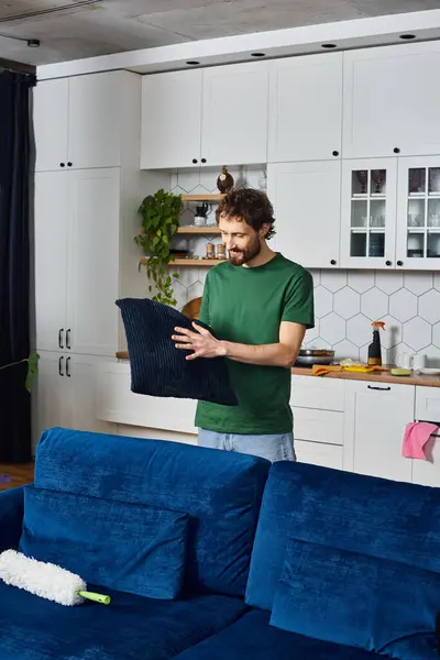 Attractive joyous man in casual green t shirt holding pillow in his hands while cleaning at home — Stock Photo
