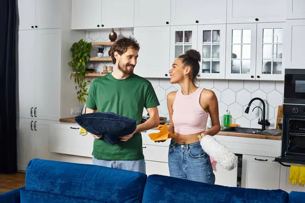 Joyous loving multicultural couple in casual attire smiling at each other during cleaning their home — Stock Photo