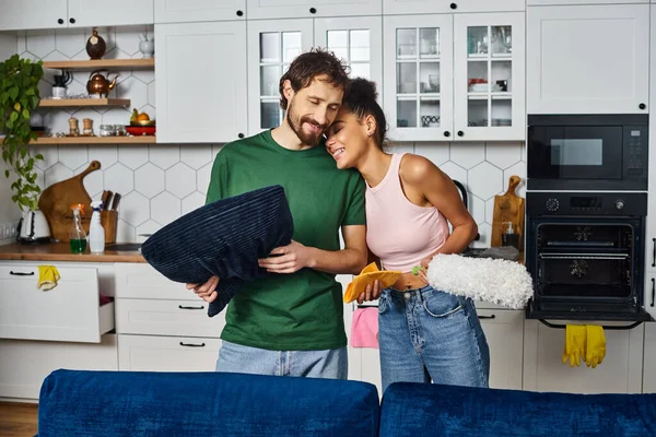 Appealing jolly multicultural couple in comfy homewear cleaning dust at home and smiling happily — Stock Photo