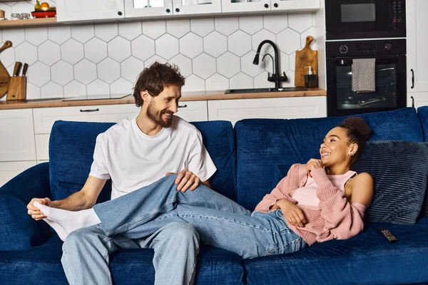 Beautiful african american woman lying on sofa next to her sitting boyfriend, smiling at each other — Stock Photo