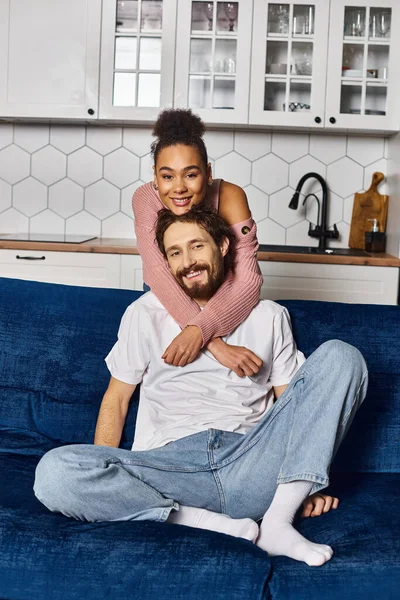 Appealing cheerful diverse couple in casual cozy attires hugging and looking at camera while at home — Stock Photo