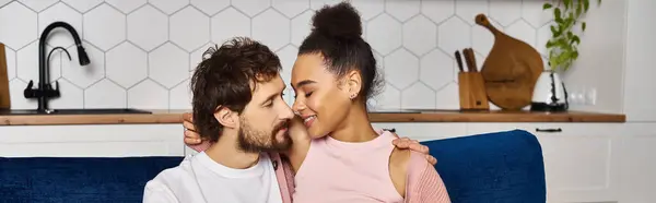 Alegre diverso casal no confortável homewear sentado no sofá juntos e sorrindo um para o outro, banner — Stock Photo