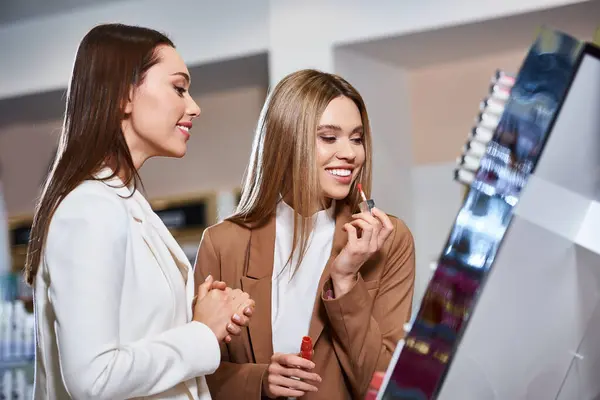 Joyous appealing women in business casual attires choosing new lipstick in cosmetics store — Stock Photo