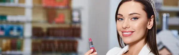 Joyous good looking woman in business casual choosing lipstick and smiling at camera, banner — Stock Photo