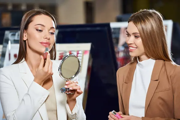 Deux joyeux belles femmes en affaires tenues décontractées choisir nouveau rouge à lèvres dans le magasin de cosmétiques — Photo de stock