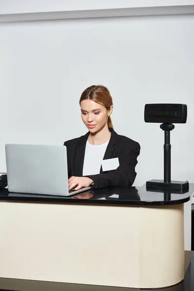 Appealing stylish saleswoman in black blazer working on laptop while sitting at counter in store — Stock Photo