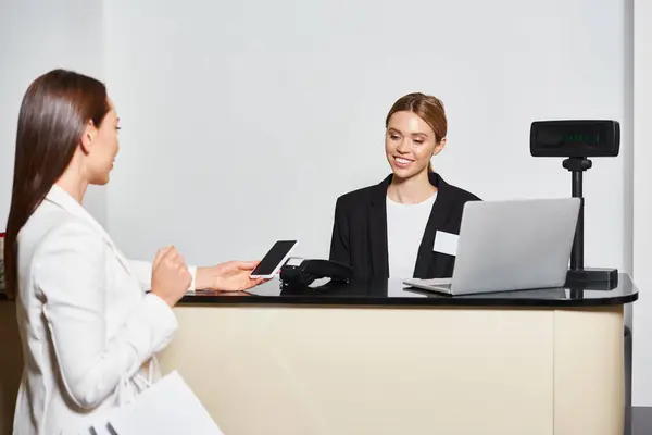 Good looking customer paying with her phone in cosmetics store with saleswoman looking at her — Stock Photo