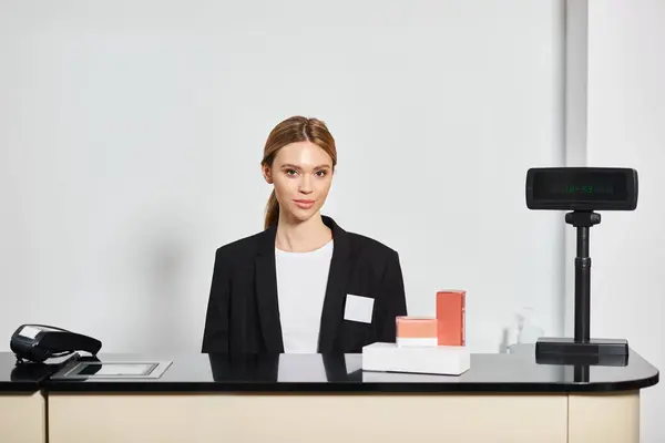 Good looking shop assistant in sophisticated black blazer sitting at counter and looking at camera — Stock Photo