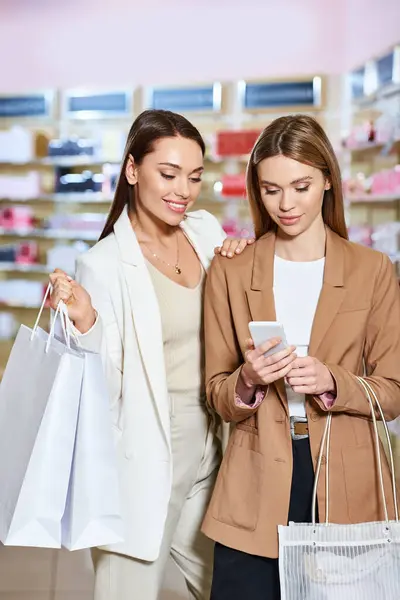 Beautiful stylish women in business casual attire looking at smartphone while in cosmetics store — Stock Photo