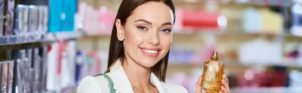 Cheerful appealing woman choosing perfumes in cosmetics store and smiling at camera, banner — Stock Photo