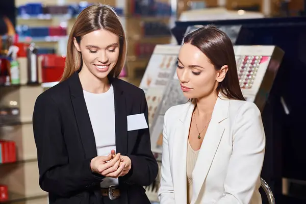 Attractive shop assistant in black blazer showing lipstick to her customer while in cosmetics store — Stock Photo