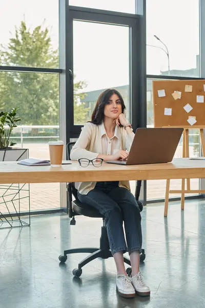 Una donna d'affari moderna siede alla sua scrivania, concentrata sul suo computer portatile in un ambiente ufficio contemporaneo. — Foto stock