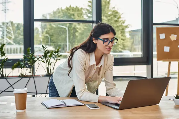 Une femme d'affaires est assise à une table, concentrée sur son ordinateur portable dans un cadre de bureau moderne, incarnant l'essence du travail de franchise. — Photo de stock