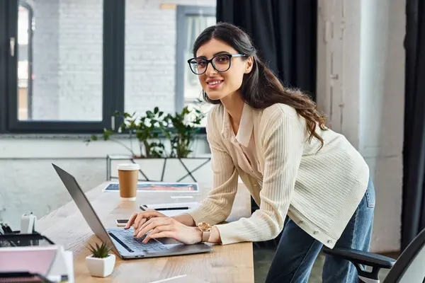 Una mujer de negocios determinada se sienta en un escritorio, la estrategia de expansión de franquicia utilizando un ordenador portátil en una oficina moderna. - foto de stock
