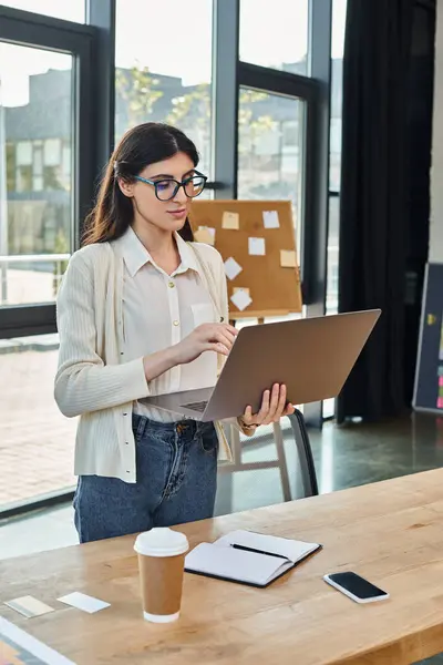 A businesswoman stands confidently in front of a laptop in a modern office setting, embodying the franchise concept. — Stock Photo