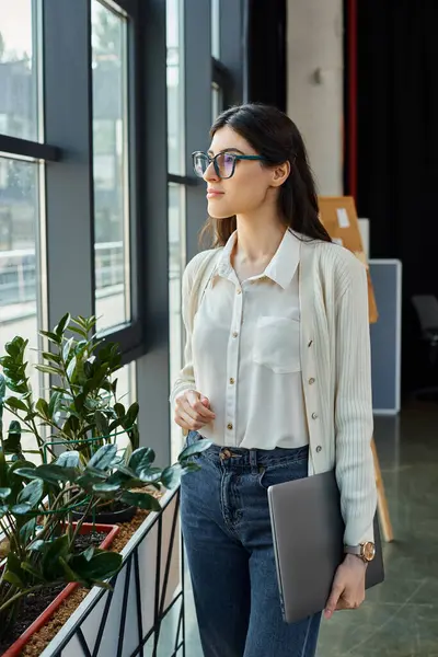 A businesswoman stands by a window, holding a folder in a modern office space. — Stock Photo