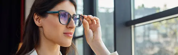 Uma empresária confiante vestindo óculos de sol elegantes olha para fora de uma janela em um espaço de escritório moderno, refletindo sobre seu sucesso e jornada empresarial. — Fotografia de Stock