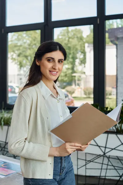 A businesswoman examines a clipboard by a sleek window in a modern office, embodying a pioneering franchise concept. — Stock Photo