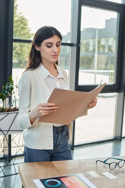 A businesswoman stands in a modern office, holding a piece of paper, with a table in the background hinting at a franchise concept. — Stock Photo