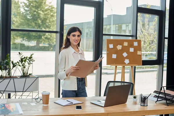 Eine Geschäftsfrau steht selbstbewusst an ihrem Schreibtisch und hält ein wichtiges Dokument in der Hand. — Stockfoto