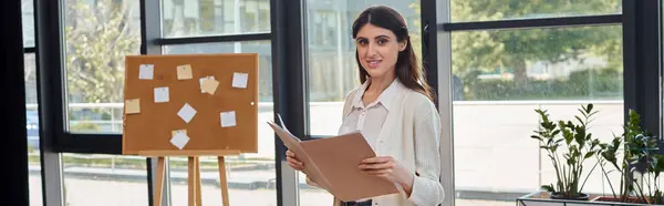 Une femme d'affaires moderne tient un papier à côté d'une planche, réfléchissant à des idées créatives dans un espace de bureau contemporain. — Photo de stock
