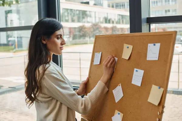 A dynamic female entrepreneur stands confidently in front of a board filled with strategic plans and ideas in a modern office space. — Stock Photo