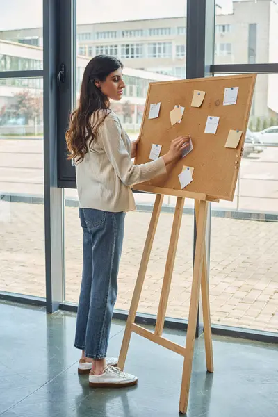 A businesswoman stands by an board covered in post-it notes, strategizing franchise concepts in a modern office. — Stock Photo