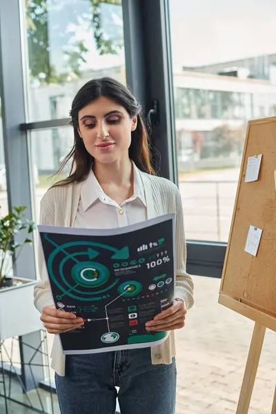 A modern businesswoman stands confidently near board, holding charts in a modern office workspace, embodying the franchise concept. — Stock Photo