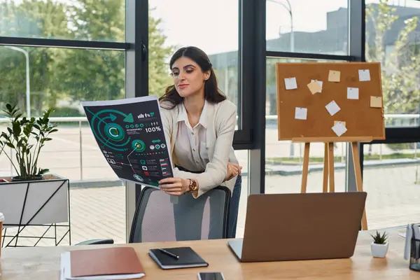 Eine Geschäftsfrau in einem modernen Büroraum, in Gedanken vertieft, während sie am Schreibtisch Diagramme liest. — Stockfoto
