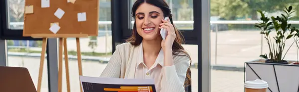 Бізнес-леді сидить за столом в сучасному офісі, займається телефонним дзвінком, демонструючи концепцію франшизи. — стокове фото