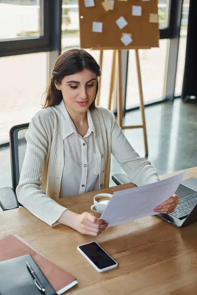 Une femme d'affaires moderne s'assoit à une table, profitant d'un moment de détente avec une tasse de café dans un cadre de bureau chic. — Photo de stock