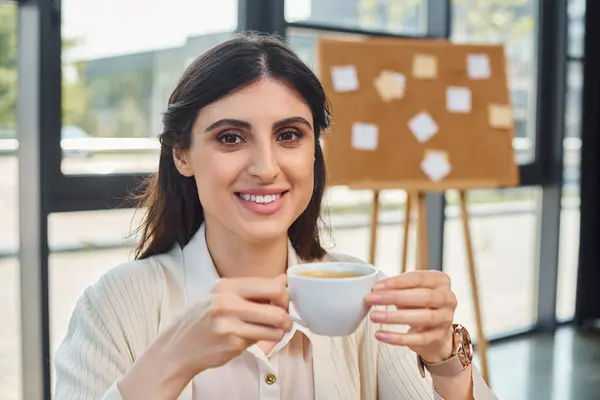 A businesswoman enjoys a peaceful moment at a table, sipping coffee in a modern office space with a franchise concept. — Stock Photo