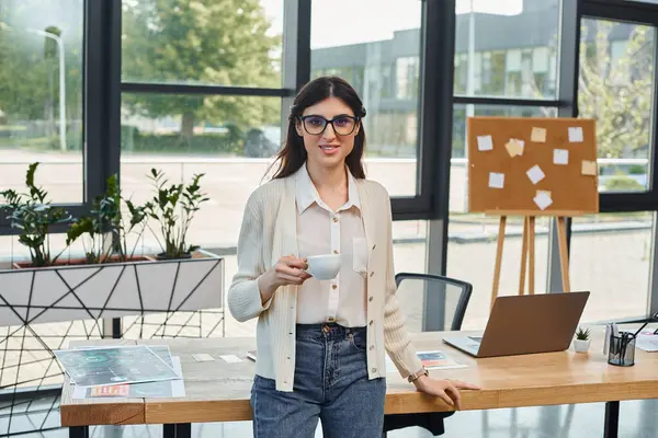 Une femme d'affaires se tient dans un bureau moderne, concentré sur son ordinateur portable sur la table devant elle. — Photo de stock