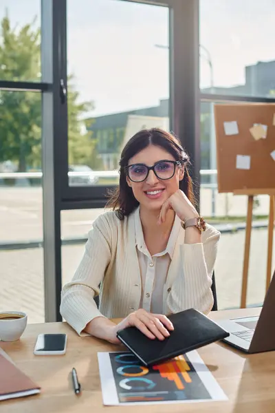 Une femme d'affaires, entourée des outils de son métier, s'assoit absorbée dans son travail à une table moderne. — Photo de stock