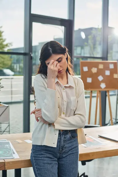 Uma mulher de negócios está na frente de uma mesa segurando a cabeça, contemplando seu sucesso de franquia em um escritório moderno. — Fotografia de Stock