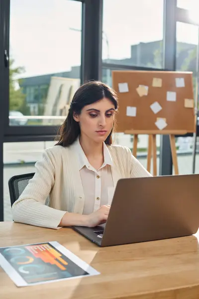 Uma mulher de negócios em um escritório moderno está sentada em uma mesa, focada em usar um laptop para o trabalho. — Fotografia de Stock