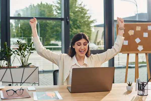 A businesswoman sitting at a desk with her arms raised in celebration of a successful franchise concept in a modern office setting. — Stock Photo