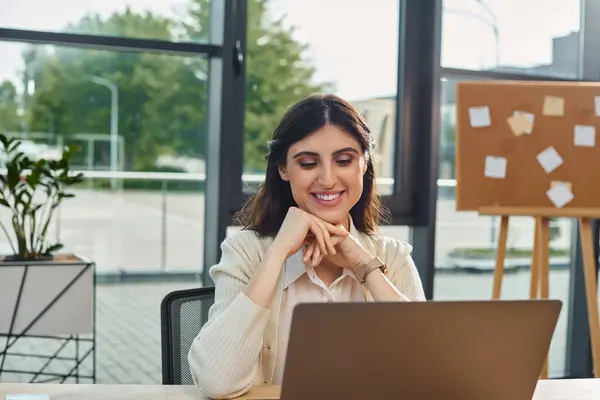 Una donna d'affari si siede di fronte a un computer portatile in un ufficio moderno, incentrato sul suo concetto di franchising lavoro. — Foto stock
