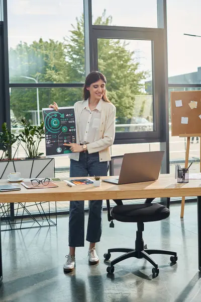 Une femme d'affaires se tient dans un bureau moderne, se concentrant sur son ordinateur portable à un bureau élégant, présentant le concept de franchise. — Photo de stock