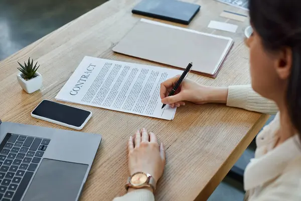A businesswoman in a modern office, sitting at a table with a laptop and papers, immersed in her work. — Stock Photo