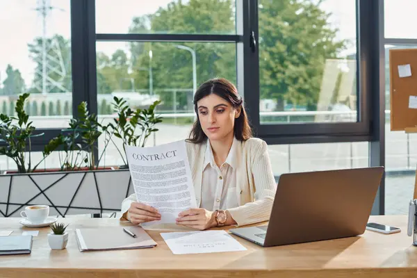 Une femme d'affaires s'assoit à un bureau, se concentrant sur la lecture d'un contrat, incarnant l'essence de la planification stratégique dans un cadre de bureau moderne. — Photo de stock