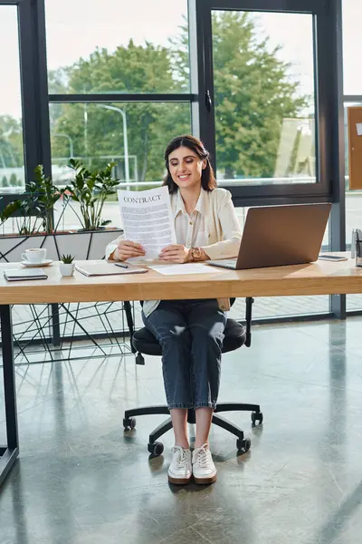 Una mujer de negocios sentada en un escritorio en una oficina moderna, absorta en el trabajo en su computadora portátil, encarnando un concepto de franquicia. - foto de stock