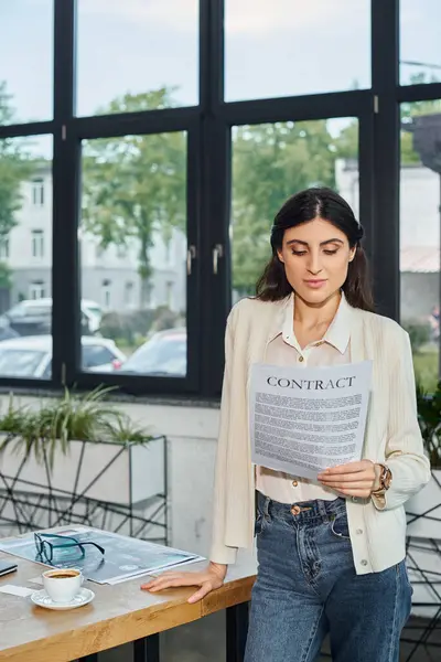 A businesswoman stands by a table, holding a contract, in a modern office setting representing a franchise concept. — Stock Photo