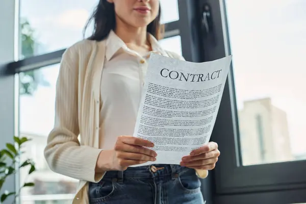 Une femme d'affaires se tient près d'une fenêtre, détenant un contrat dans un cadre de bureau moderne. — Photo de stock
