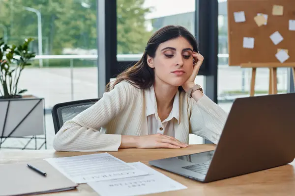 Una donna d'affari siede a un tavolo in un ufficio moderno, focalizzato sul suo computer portatile, incarnando il concetto di un fiorente franchising.. — Foto stock