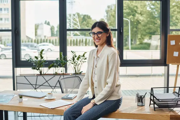 Une femme d'affaires concentrée assise sur une table avec un ordinateur portable, réfléchissant aux stratégies de franchise dans un bureau moderne. — Photo de stock