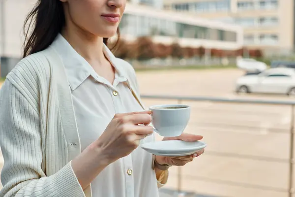 A businesswoman gracefully holds a cup and saucer outdoors, embodying a moment of calm amidst the bustling franchise concept of a modern office. — Stock Photo