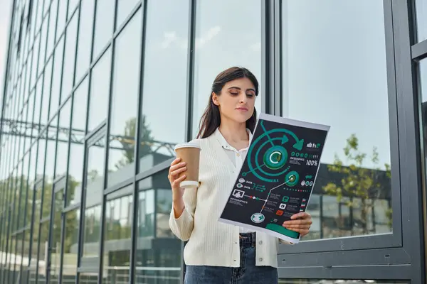 Une femme d'affaires dans un cadre moderne de bureau en plein air, tenant une tasse de café et des graphiques, symbolisant un équilibre entre travail et détente. — Photo de stock