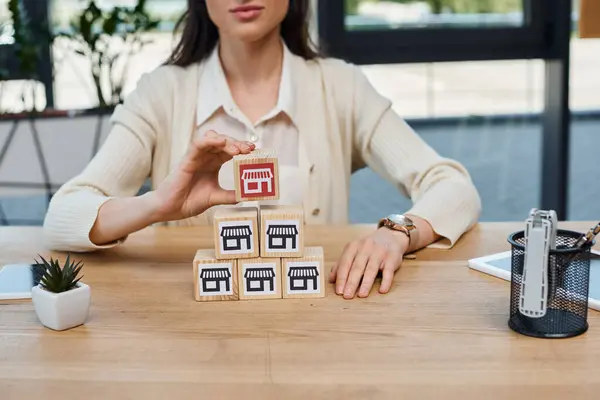 Una mujer de negocios en una oficina moderna sentada en una mesa con un montón de bloques, participando en un concepto de franquicia. - foto de stock
