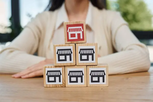 A determined businesswoman sits at a table, focused on arranging a stack of blocks, symbolizing her strategic approach to growing a franchise. — Stock Photo